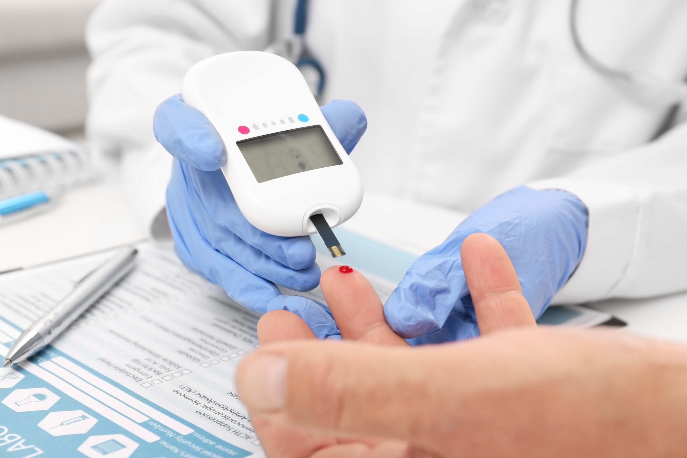 A gloved clinician checks a patient's blood glucose with a digital glucometer during an on-site lab test