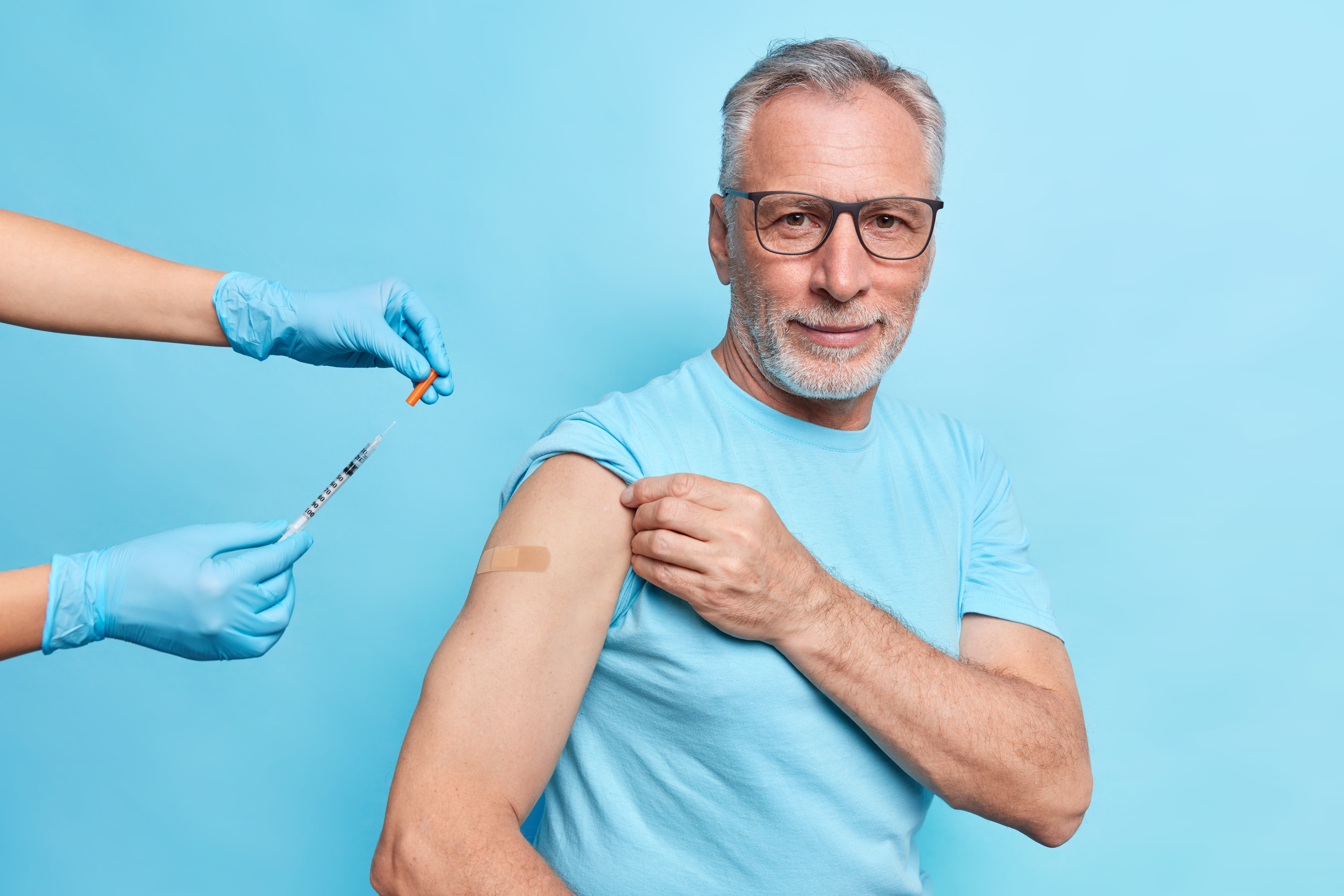 A smiling older man shows the bandage on his upper arm after getting his flu shot