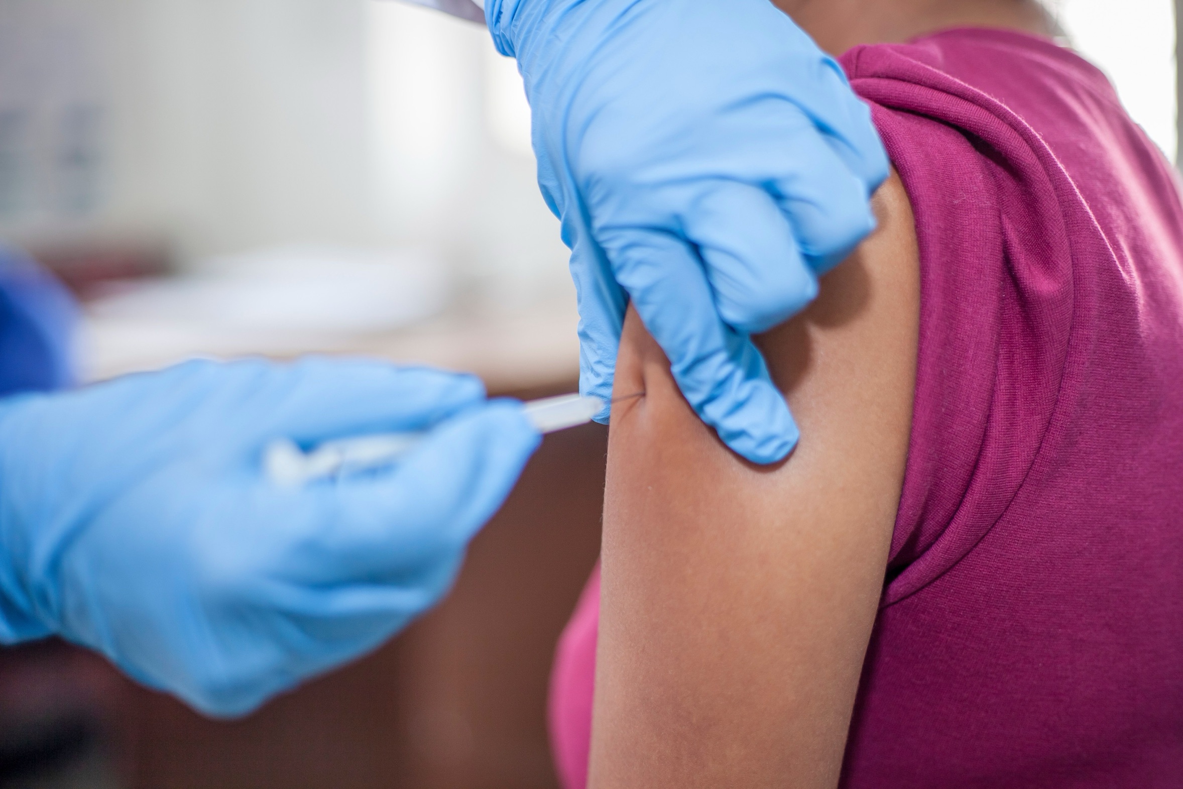 A health care worker in blue gloves gives a flu shot in a patient's upper arm