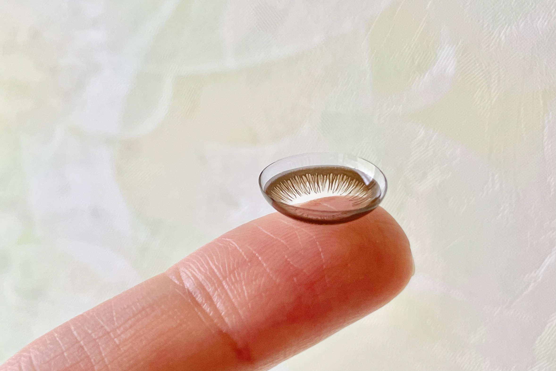 A coloured costume contact lens balanced on a fingertip, ready to be put in